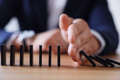 Photo of Risk. Man stopping domino effect at table, closeup
