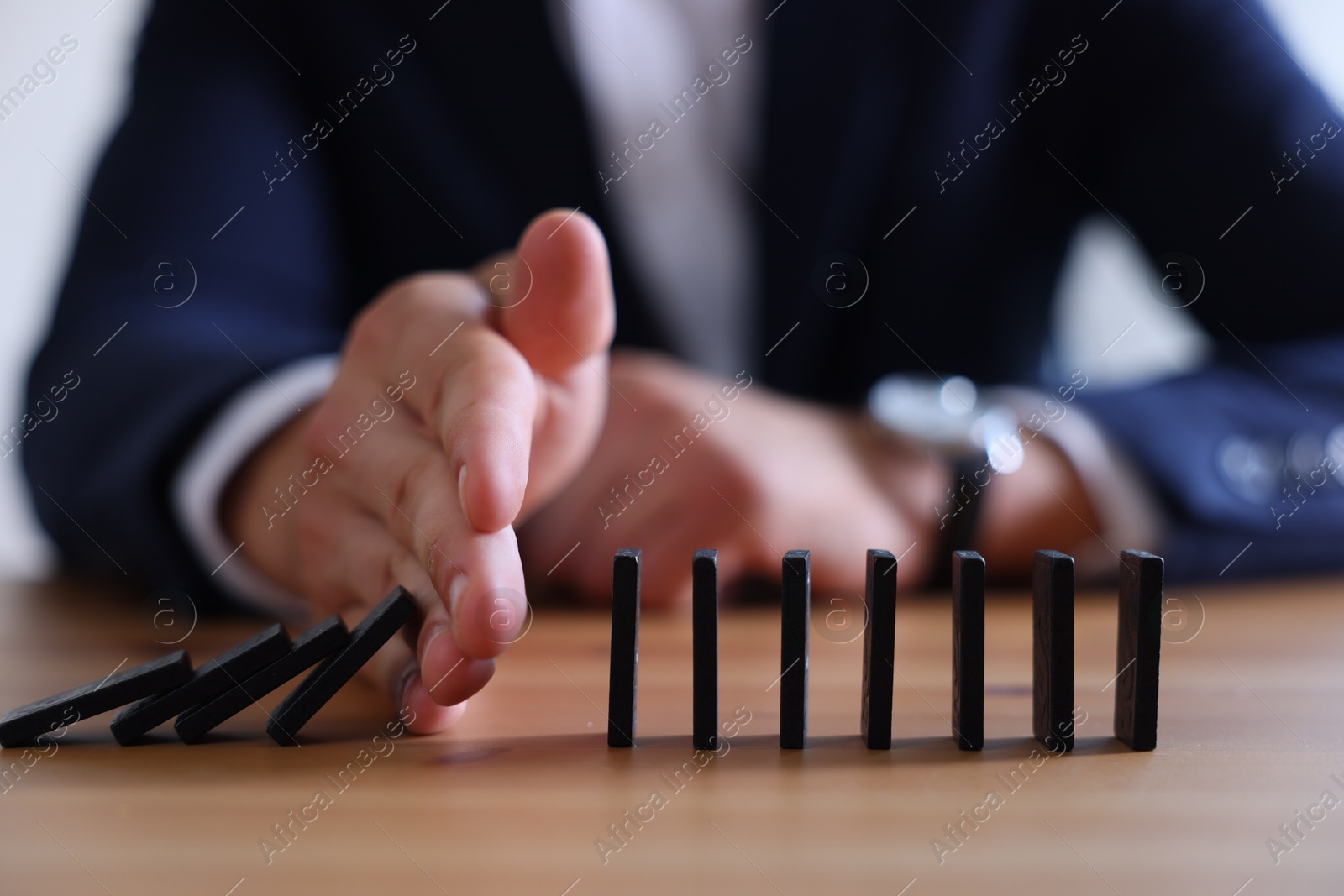 Photo of Risk. Man stopping domino effect at table, closeup