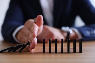 Photo of Risk. Man stopping domino effect at table, closeup