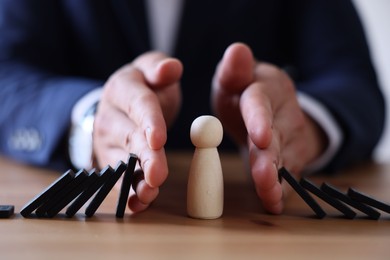 Photo of Risk. Man stopping domino effect to protect wooden figure at table, closeup