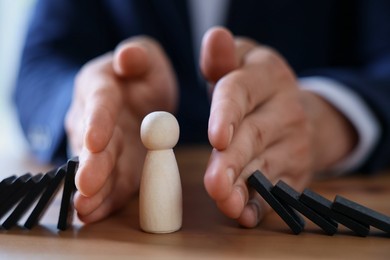 Photo of Risk. Man stopping domino effect to protect wooden figure at table, closeup
