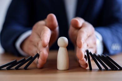 Photo of Risk. Man stopping domino effect to protect wooden figure at table, closeup