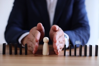 Photo of Risk. Man stopping domino effect to protect wooden figure at table, closeup