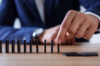 Photo of Risk. Man taking domino tale at wooden table, closeup