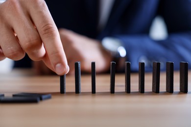 Photo of Risk. Man taking domino tale at wooden table, closeup