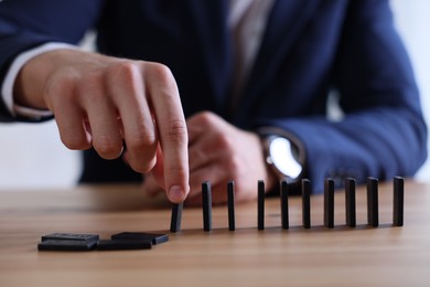 Photo of Risk. Man taking domino tale at wooden table, closeup