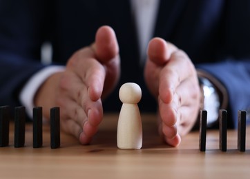 Photo of Risk. Man stopping domino effect to protect wooden figure at table, closeup