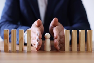 Photo of Risk. Man stopping domino effect to protect wooden figure at table, closeup