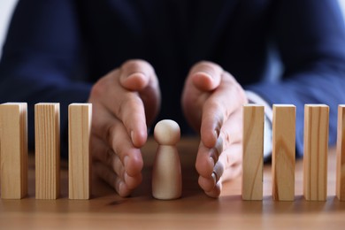 Photo of Risk. Man stopping domino effect to protect wooden figure at table, closeup