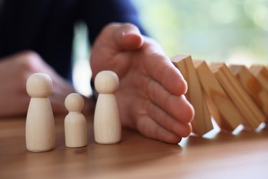 Photo of Risk. Man stopping domino effect to protect wooden figures at table, closeup