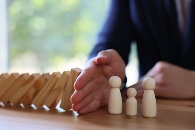 Photo of Risk. Man stopping domino effect to protect wooden figures at table, closeup