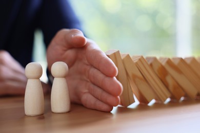 Photo of Risk. Man stopping domino effect to protect wooden figures at table, closeup