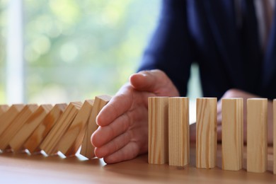 Photo of Risk. Man stopping domino effect at wooden table, closeup
