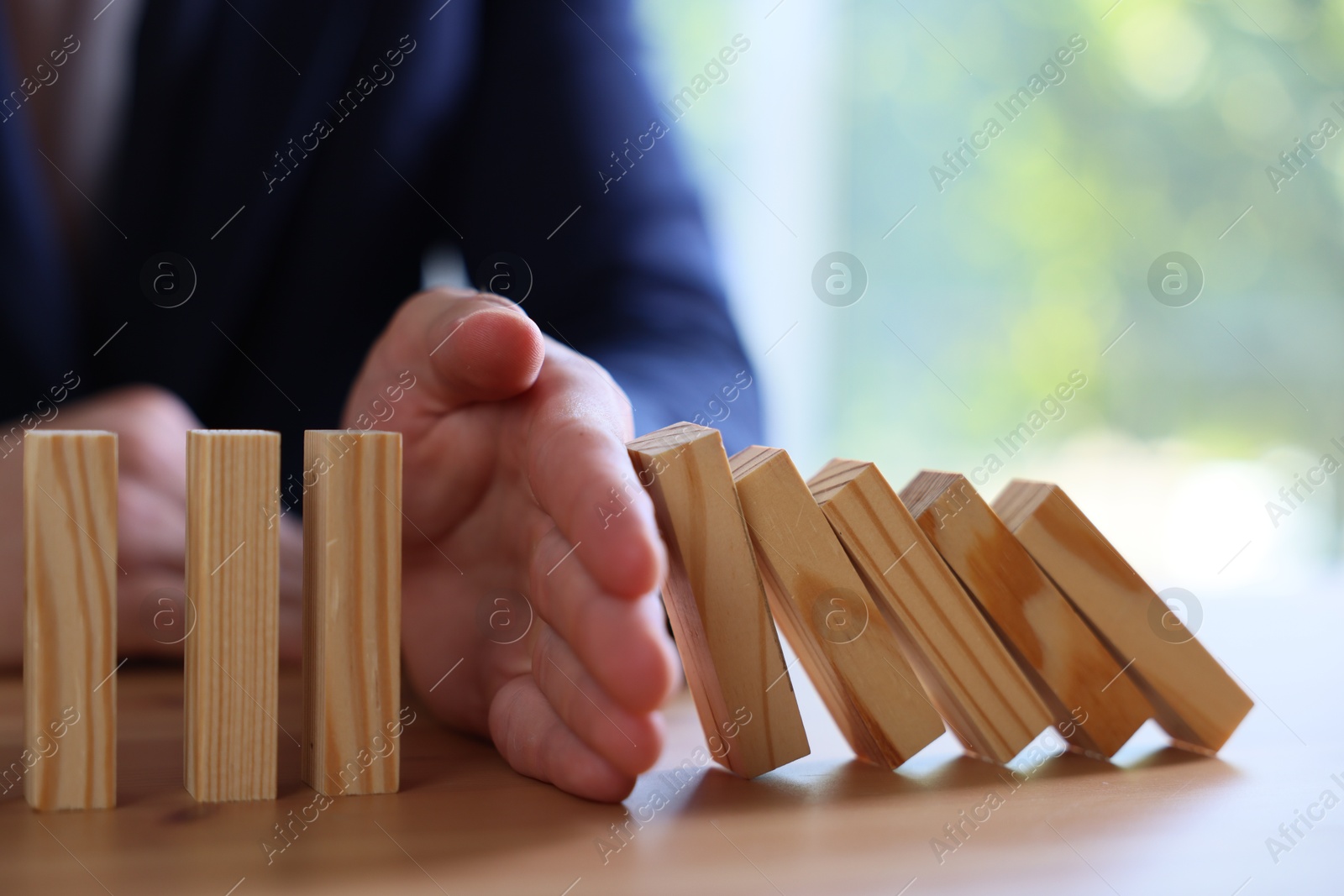 Photo of Risk. Man stopping domino effect at wooden table, closeup
