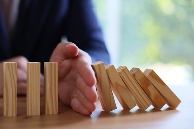 Photo of Risk. Man stopping domino effect at wooden table, closeup