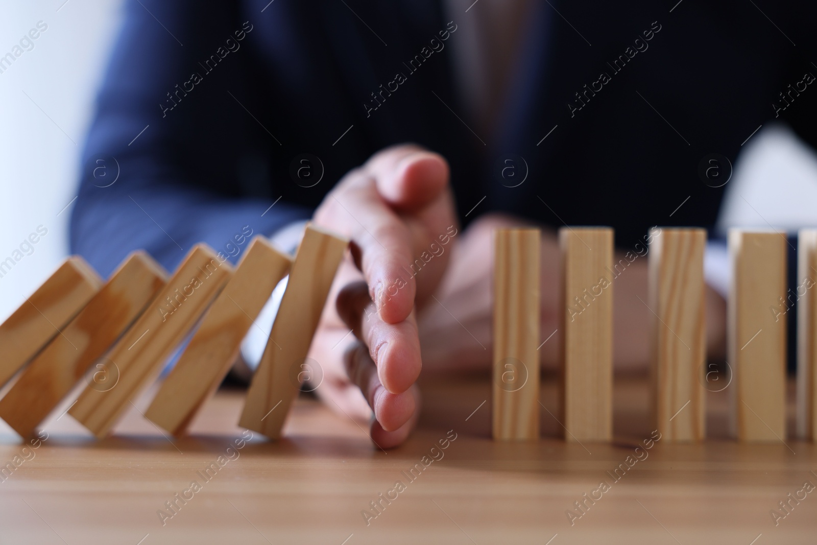 Photo of Risk. Man stopping domino effect at wooden table, closeup