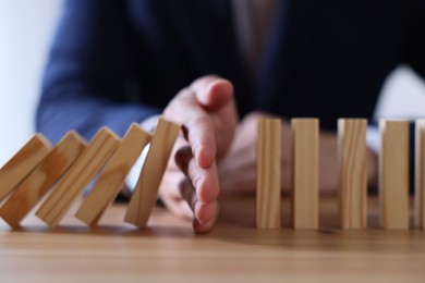Photo of Risk. Man stopping domino effect at wooden table, closeup