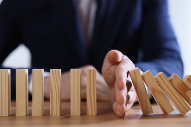 Photo of Risk. Man stopping domino effect at wooden table, closeup
