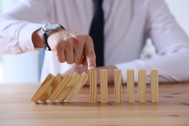 Photo of Risk. Man stopping domino effect at wooden table, closeup