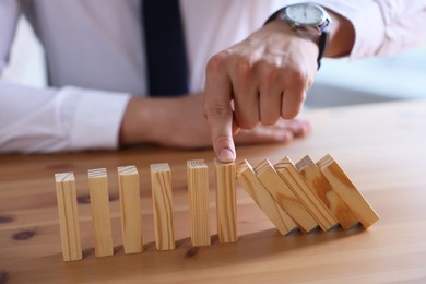 Photo of Risk. Man stopping domino effect at wooden table, closeup