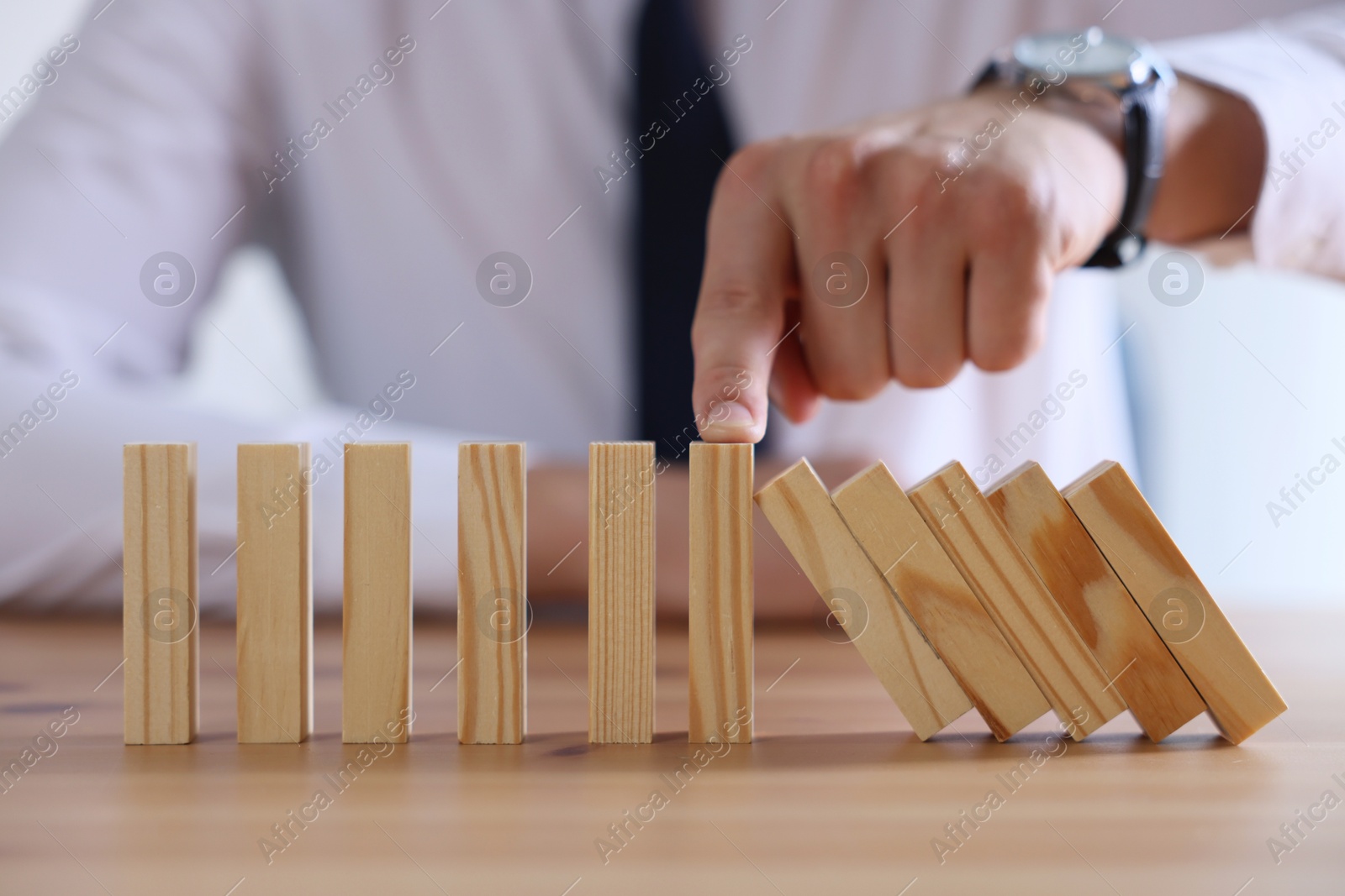 Photo of Risk. Man stopping domino effect at wooden table, closeup
