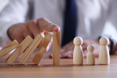 Photo of Risk. Man stopping domino effect to protect wooden figures at table, closeup