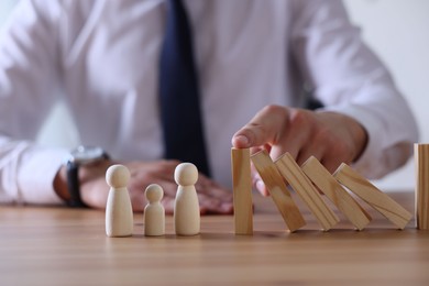 Photo of Risk. Man stopping domino effect to protect wooden figures at table, closeup