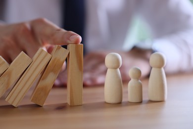 Photo of Risk. Man stopping domino effect to protect wooden figures at table, closeup