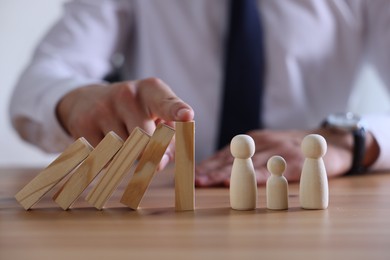 Photo of Risk. Man stopping domino effect to protect wooden figures at table, closeup