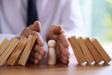 Photo of Risk. Man stopping domino effect to protect wooden figure at table, closeup