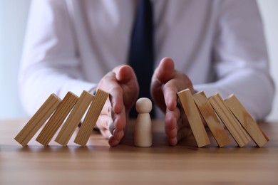 Photo of Risk. Man stopping domino effect to protect wooden figure at table, closeup