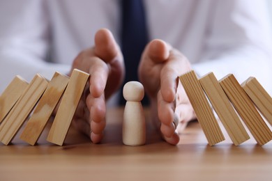 Photo of Risk. Man stopping domino effect to protect wooden figure at table, closeup