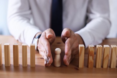 Photo of Risk. Man stopping domino effect to protect wooden figure at table, closeup