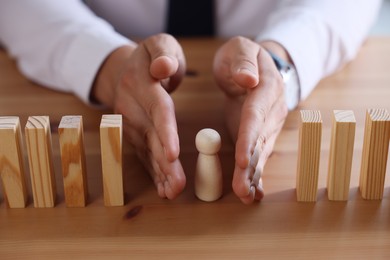 Photo of Risk. Man stopping domino effect to protect wooden figure at table, closeup
