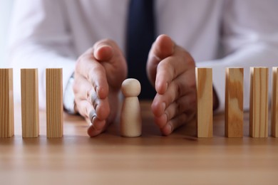 Photo of Risk. Man stopping domino effect to protect wooden figure at table, closeup