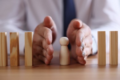 Photo of Risk. Man stopping domino effect to protect wooden figure at table, closeup