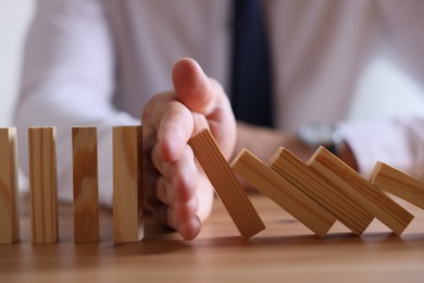 Photo of Risk. Man stopping domino effect at wooden table, closeup
