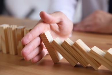 Photo of Risk. Man stopping domino effect at wooden table, closeup