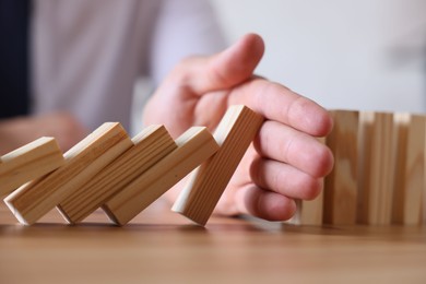 Photo of Risk. Man stopping domino effect at wooden table, closeup