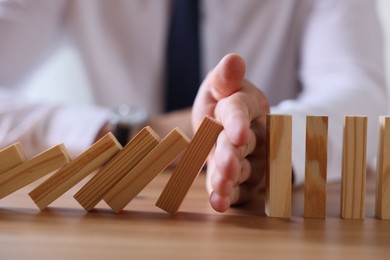 Photo of Risk. Man stopping domino effect at wooden table, closeup