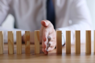 Photo of Risk. Man stopping domino effect at wooden table, closeup