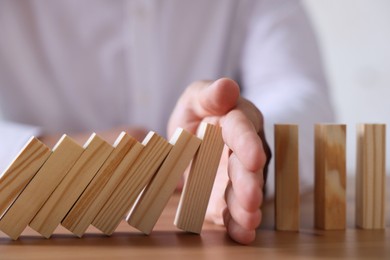 Photo of Risk. Man stopping domino effect at wooden table, closeup