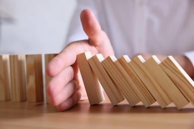 Photo of Risk. Man stopping domino effect at wooden table, closeup
