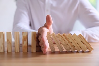 Photo of Risk. Man stopping domino effect at wooden table, closeup