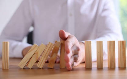 Photo of Risk. Man stopping domino effect at wooden table, closeup