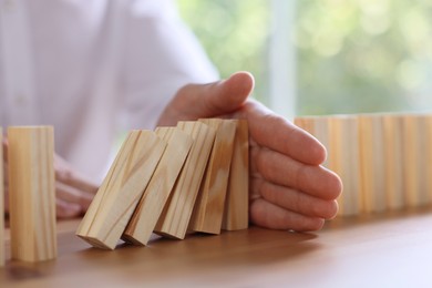 Photo of Risk. Man stopping domino effect at wooden table, closeup