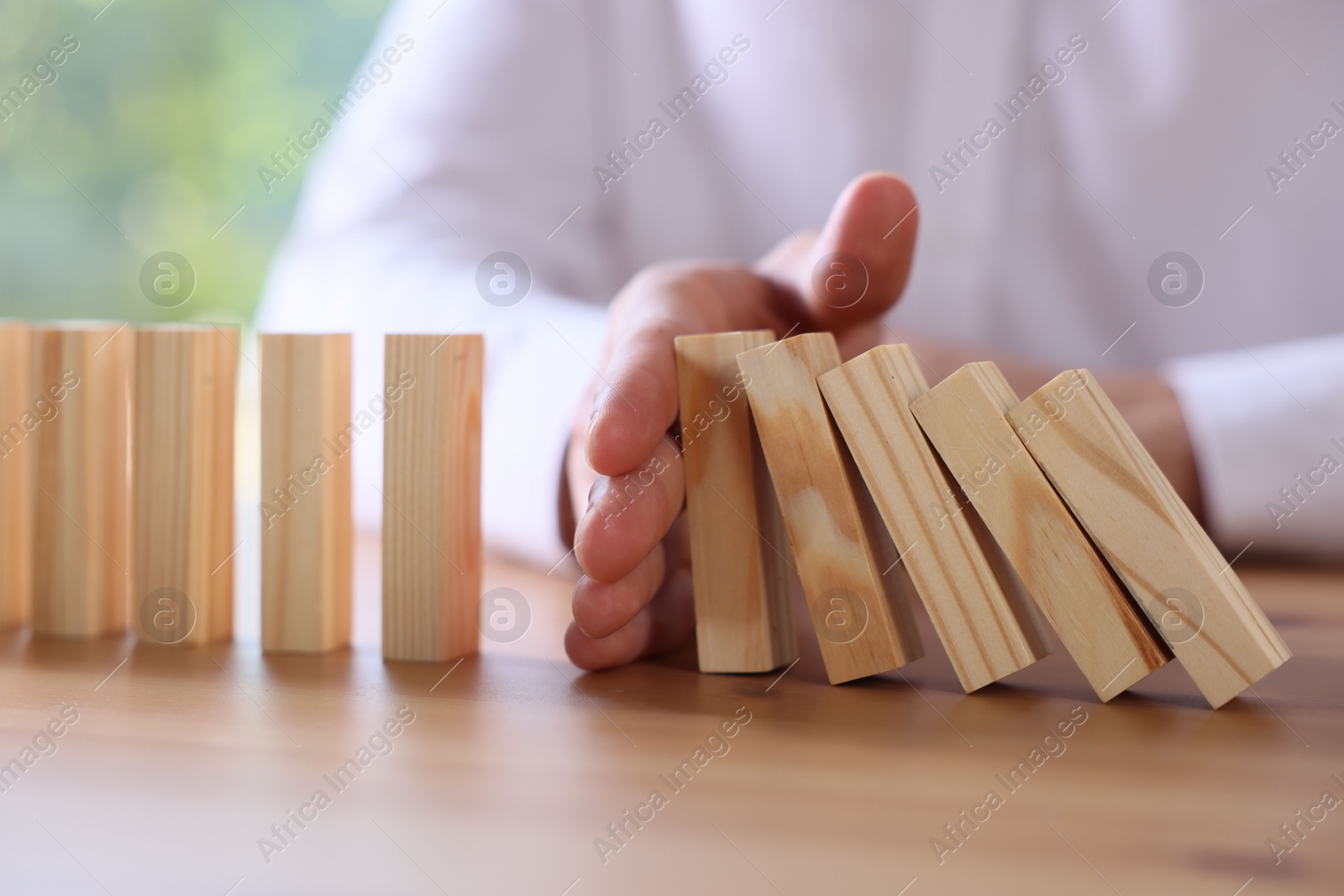 Photo of Risk. Man stopping domino effect at wooden table, closeup