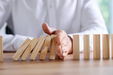 Photo of Risk. Man stopping domino effect at wooden table, closeup