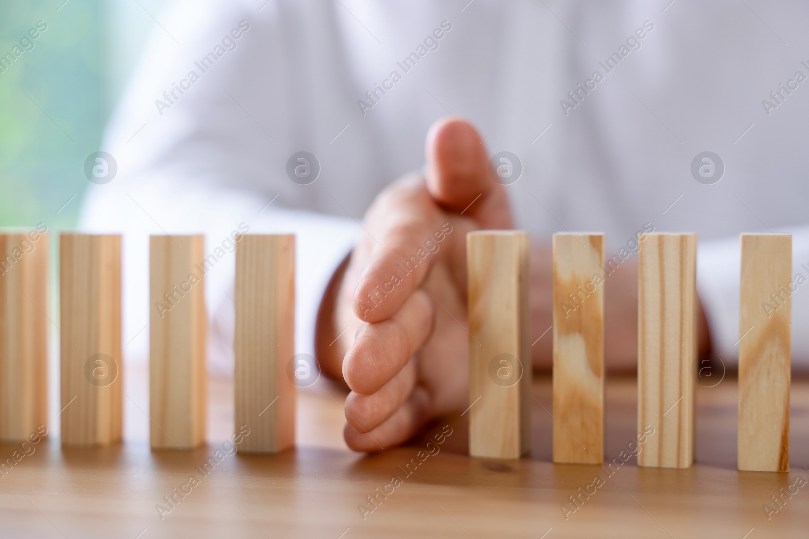 Photo of Risk. Man stopping domino effect at wooden table, closeup