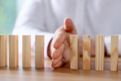 Photo of Risk. Man stopping domino effect at wooden table, closeup